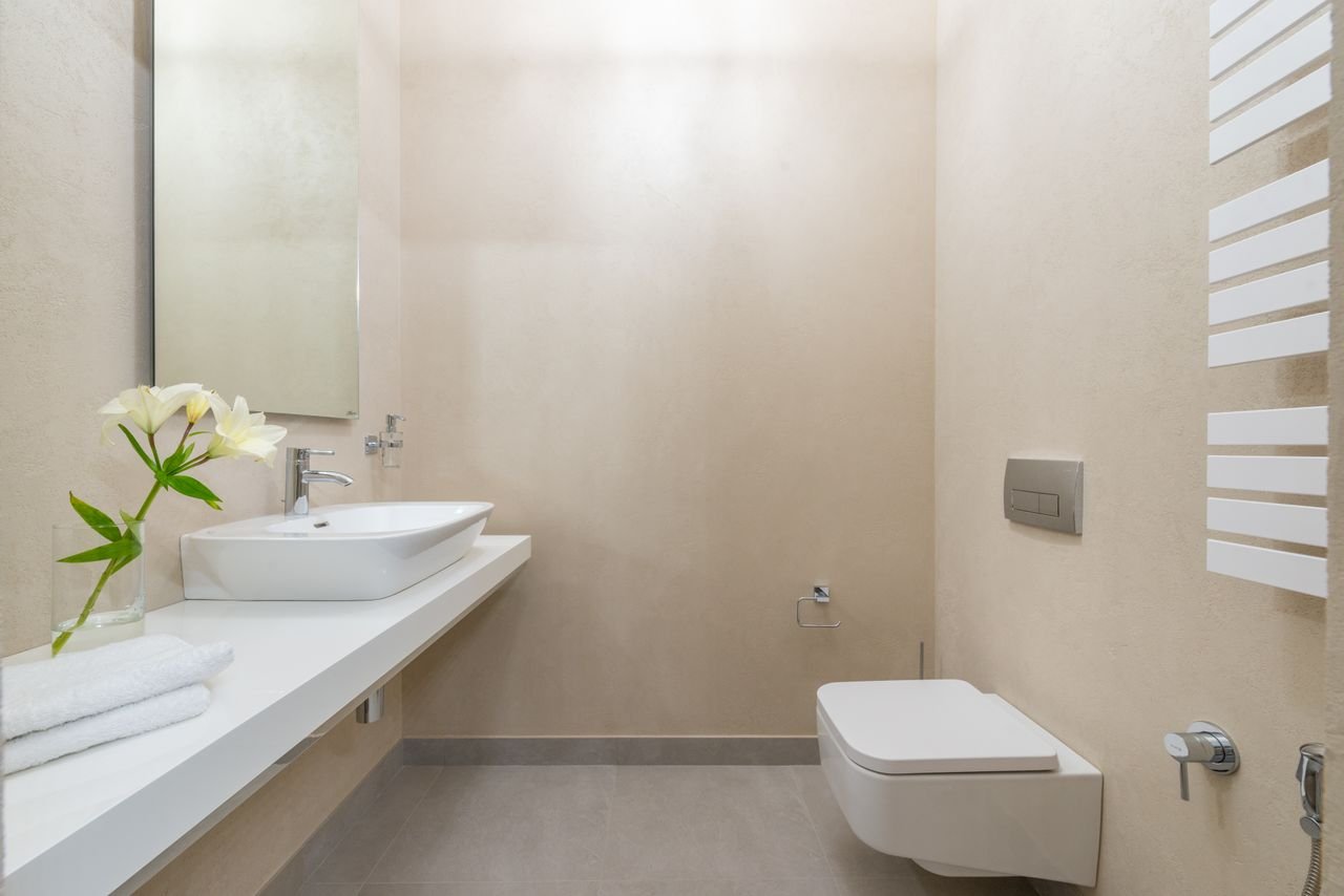 White ceramic toilet placed against wall with mirror and sink near blooming white flowers and towels in light modern bathroom