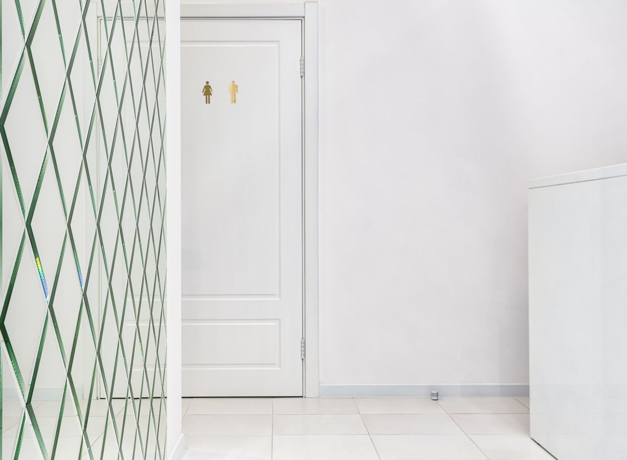 Interior of empty hallway with tiled floor white door of bathroom and glass wall with geometric elements